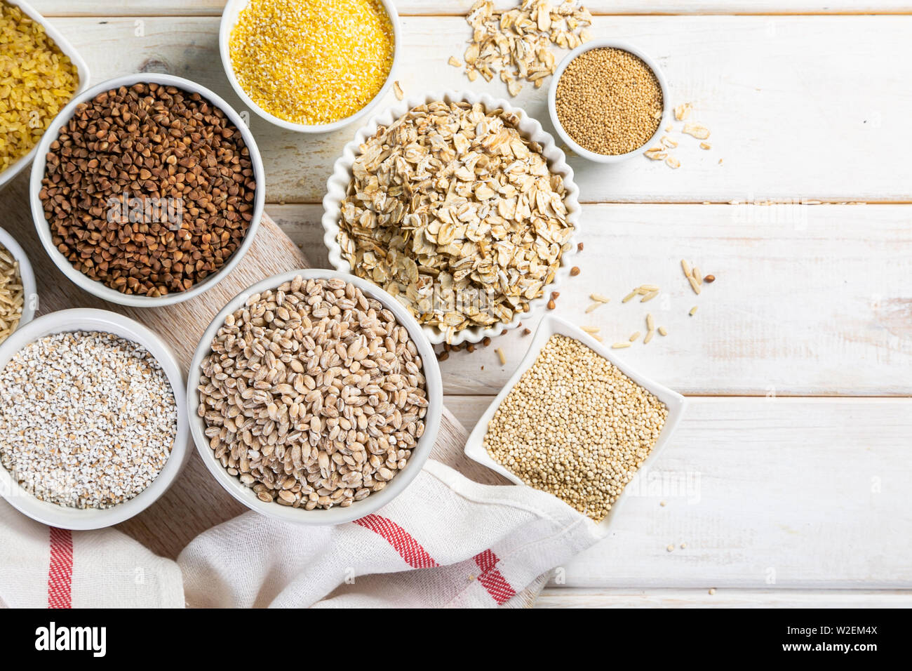 Auswahl von Vollkornprodukten in weißen Schalen - Reis, Hafer, Buchweizen, Bulgur, Haferbrei, Gerste, Quinoa, Amaranth, Stockfoto