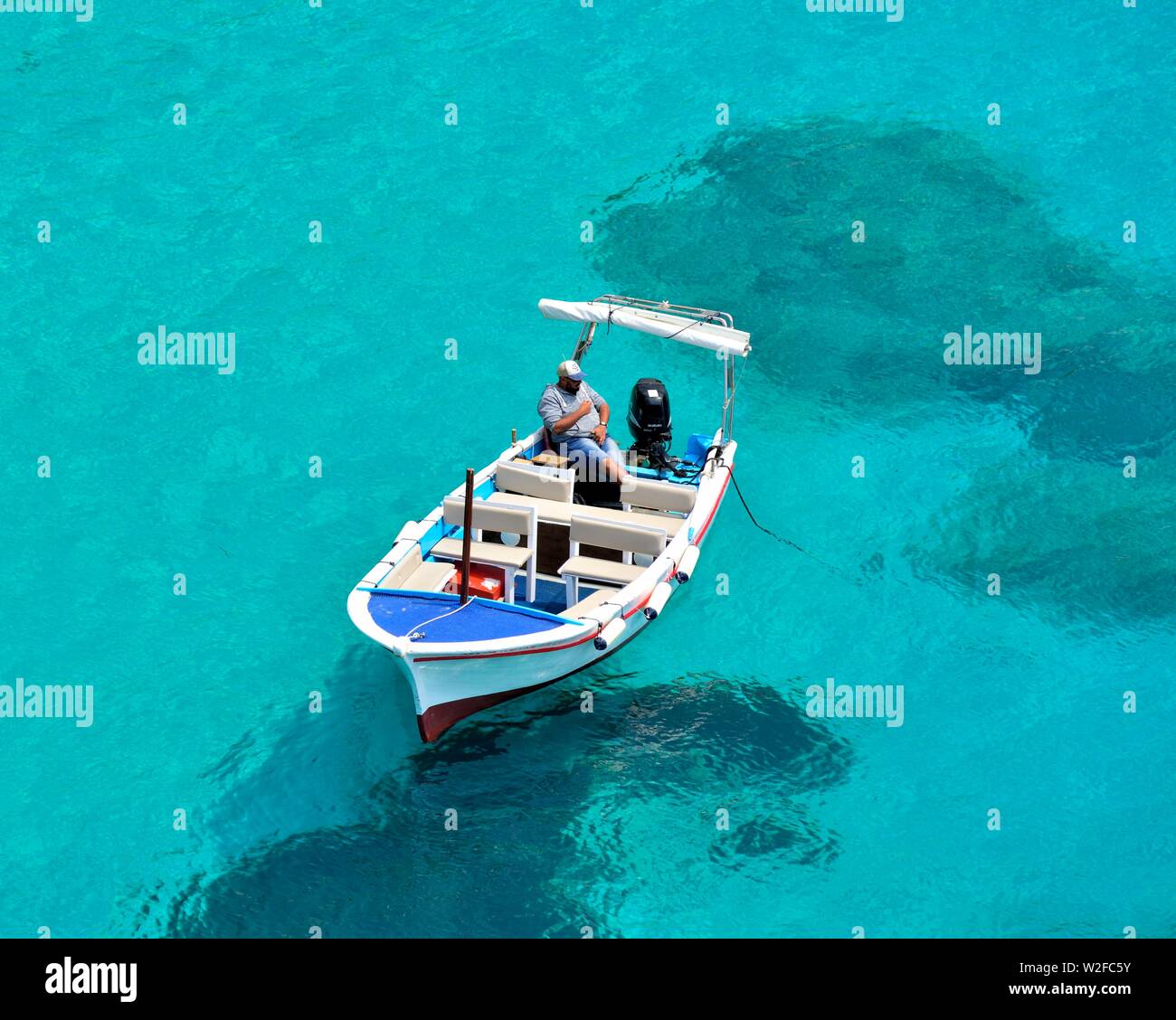 Lokale Bootsmann saß auf seinem Boot warten auf die nächste touristische Bootsfahrt, Agios Spiridon Strand, Agios Spiridon Bay, Paleokastritsa, Korfu, Griechenland, Ionian Stockfoto