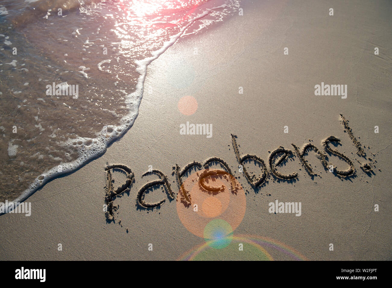 Parabene! Portugiesisch (Englische Übersetzung: Herzlichen Glückwunsch) Nachricht handschriftlich in strukturierte Schriftzug auf glatten Sand mit einer Welle an einem brasilianischen Strand Stockfoto