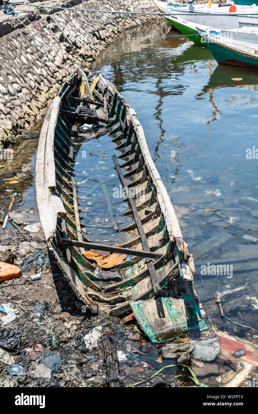 Makassar, Sulawesi, Indonesien - 28. Februar 2019: Paotere Alten Hafen. Ruinierte Skelett von kleinen Boot unter anderem Müll im Meer Wasser. Stockfoto