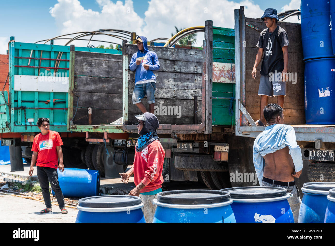 Makassar, Sulawesi, Indonesien - 28. Februar 2019: Paotere Alten Hafen. Nahaufnahme der Männer großen blauen Fässer aus öffnen Zurück Lkw entladen unter blauem Himmel. Ba Stockfoto