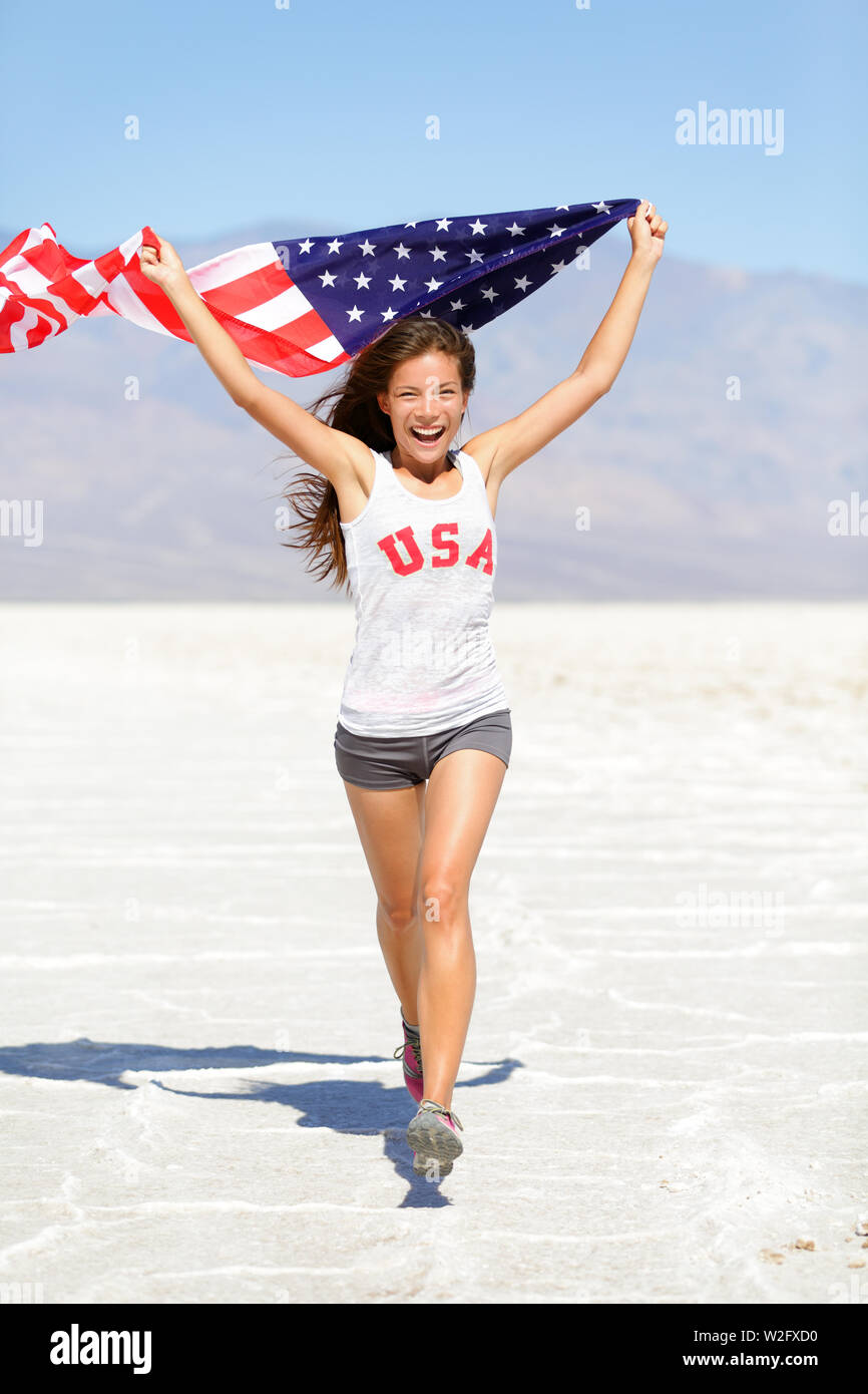 Sieger Athlet Frau läuft mit amerikanischer Flagge und USA T-Shirt. Runner girl Übersicht gewinnen Geste aufgeregt und glücklich im Freien in der Wüstenlandschaft. Freundliche fitness Frau Gewinner zujubeln, in voller Länge. Stockfoto