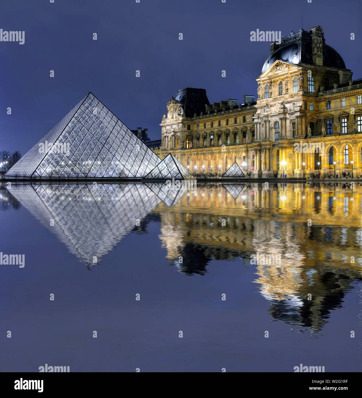 Beleuchtete Louvre Glaspyramide mit Spiegelbild im Wasser, Dämmerung, Paris, Frankreich Stockfoto