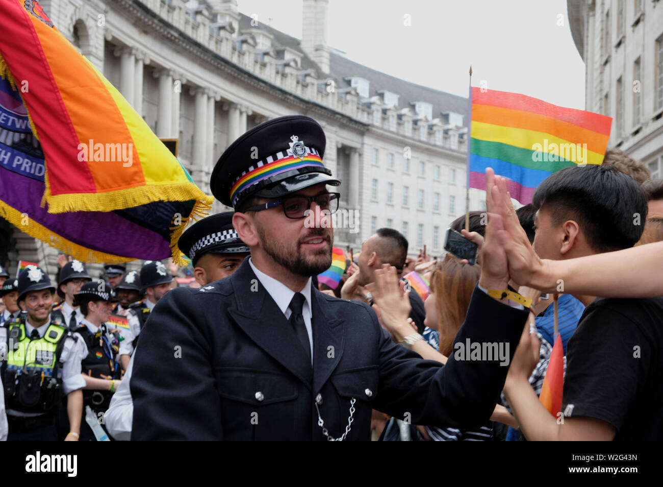 Ein Mitglieder der Metropolitan LGBT Polizei Netzwerk grüßt die Teilnehmer während der Parade. Tausende von nachtschwärmern Londons Straßen mit Farbe gefüllt Stolz in der Hauptstadt zu feiern. 2019 markierte den 50. Jahrestag der Stonewall Riots in New York City, als Ursprung der Stolz und die LGBT + rechte Bewegung angesehen. Stockfoto