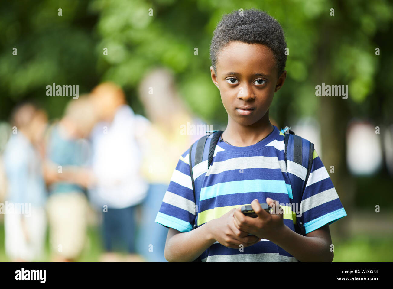 Afroamerikanische Schüler in gestreiften T-Shirt holding Telefon, während draußen vor der Schule Stockfoto