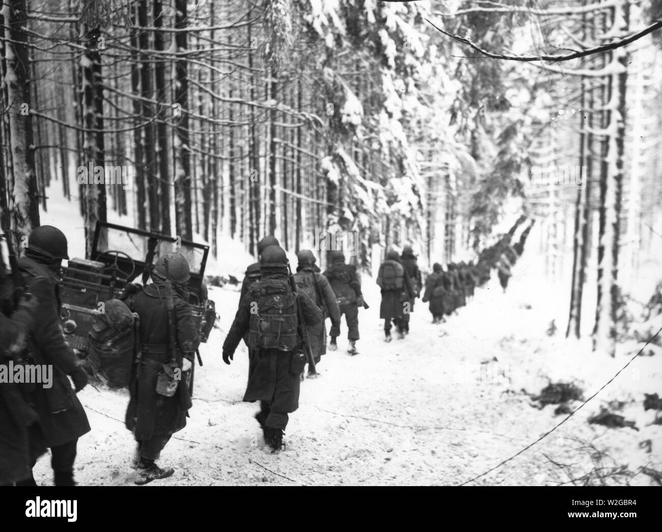 Originale Bildunterschrift: Amerikanische Soldaten der 75th Division März entlang der schneebedeckten Straße auf dem Weg von der St. Vith-Houffalize Straße in Belgien zu schneiden. 1/24/45. Stockfoto