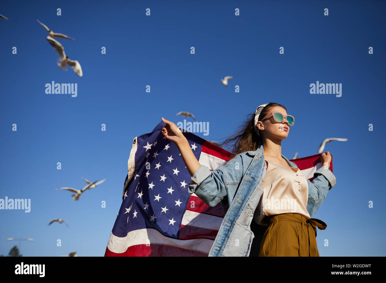 Unter der schweren stilvolle Mädchen in der Sonnenbrille und Kopftuch stehend in Wind und die amerikanische Flagge Fahne beim in die Ferne schauen, Möwen Stockfoto