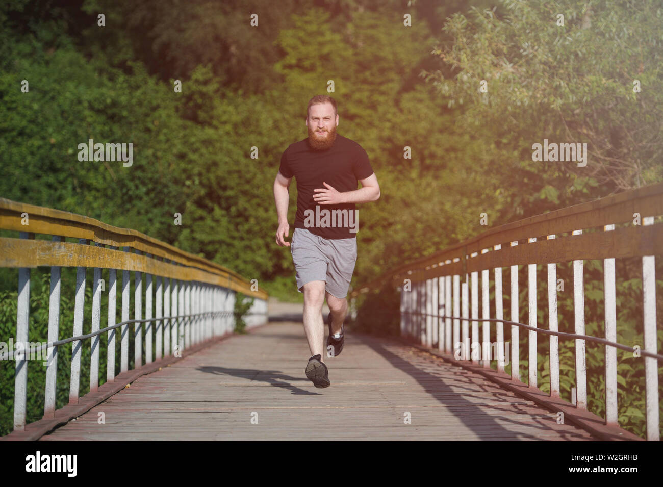 Aktive glücklichen gesunden Sport junge bärtige Männer in schwarzen T-Shirt entlang Holzbrücke in grün Sommer Park Stockfoto