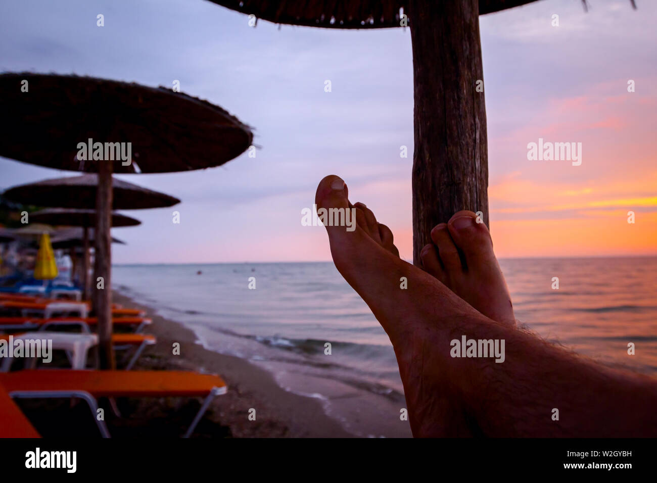 Man Beine bis zum Sonnenbaden ist liegend sorglos in Liege neben der Küste, am öffentlichen Strand. Stockfoto