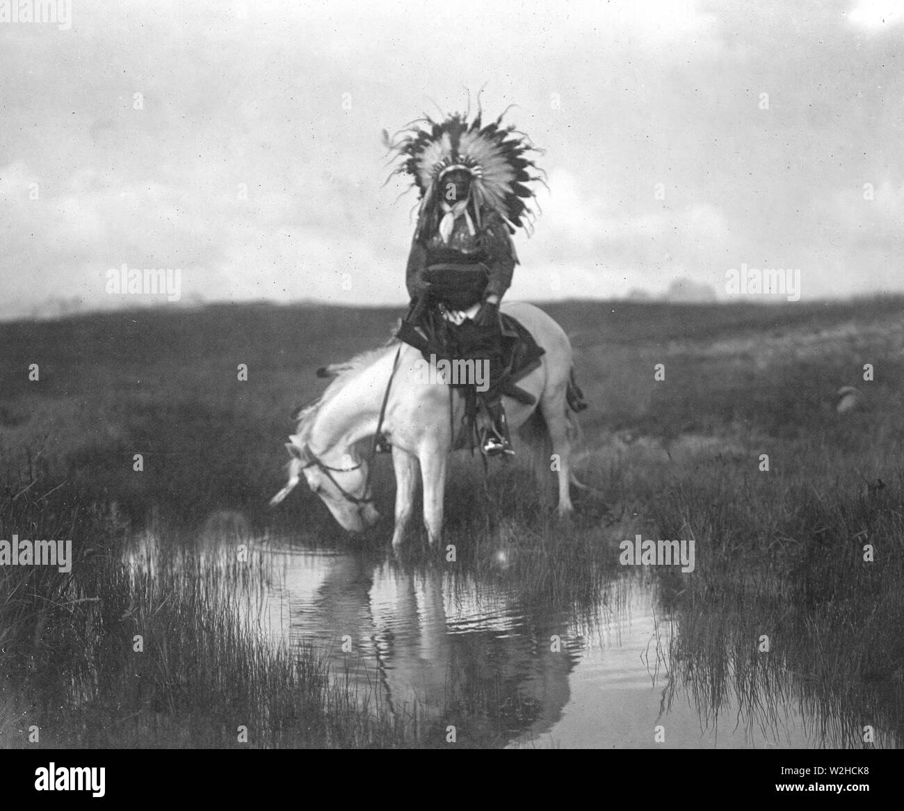 Edward S. Curtis Native American Indians - Cheyenne Indische, tragen War bonnet Kopfschmuck, auf dem Rücken der Pferde bei einem Pool von Wasser Ca. 1905 Stockfoto