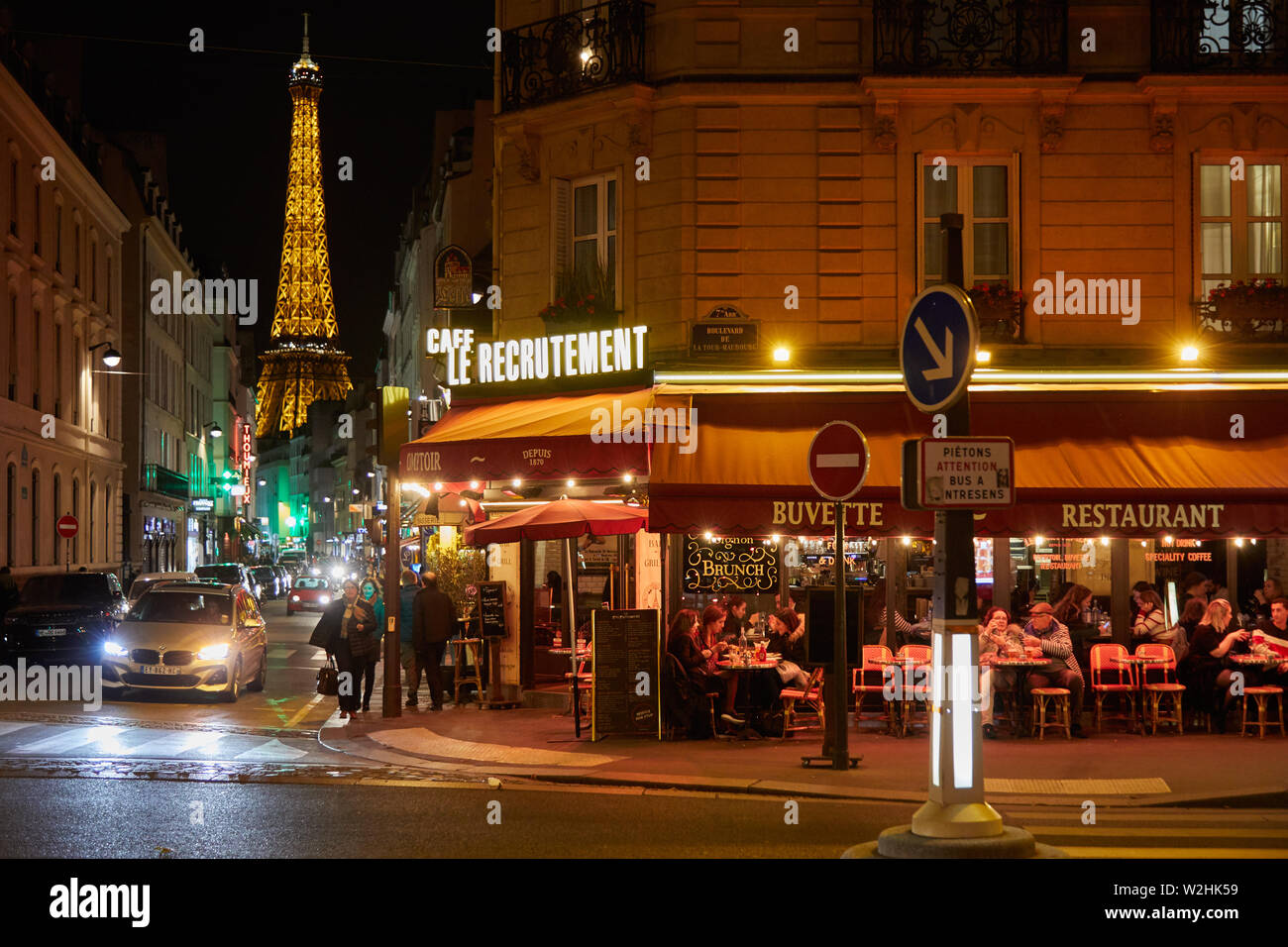 PARIS - 8. NOVEMBER 2018: Eiffelturm bei Nacht und Straße beleuchtet mit Menschen und typischen Restaurant in Paris, Frankreich Stockfoto