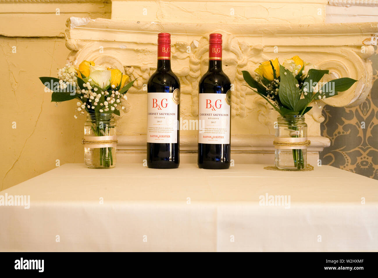 Anzeige der Tabelle mit zwei Gläser mit Blumen und zwei Flaschen von Barton & Guestier cabernet sauvignon Rotwein am 50. Hochzeitstag ein paar Party Stockfoto