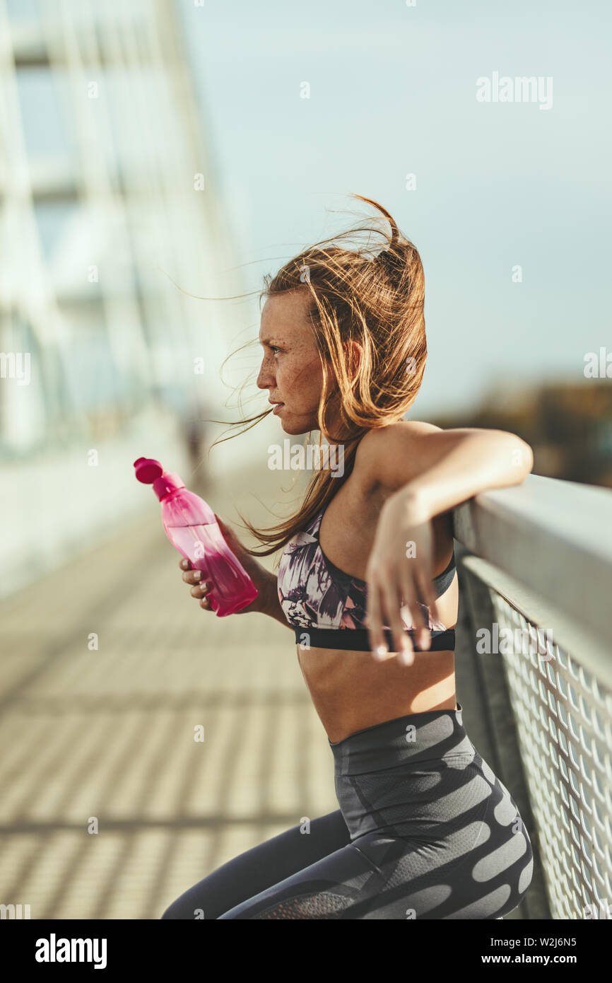 Junge fitness Frau ruht sich nach harten Training auf der Brücke über den Fluss und Trinkwasser. Stockfoto