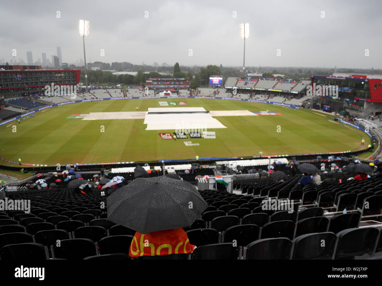 Fans sitzen unter Sonnenschirmen im steht als Regen stoppt während der ICC World Cup, Halbfinale im Emirates Old Trafford, Manchester spielen. Stockfoto