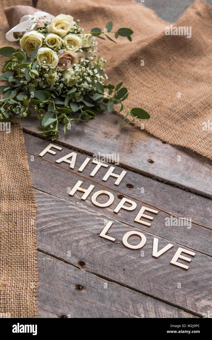 Rustikale Hintergrund mit Blumensträußen und Sackleinen mit den Worten Glauben, Hoffnung und Liebe in Holz- Buchstaben geschrieben Stockfoto