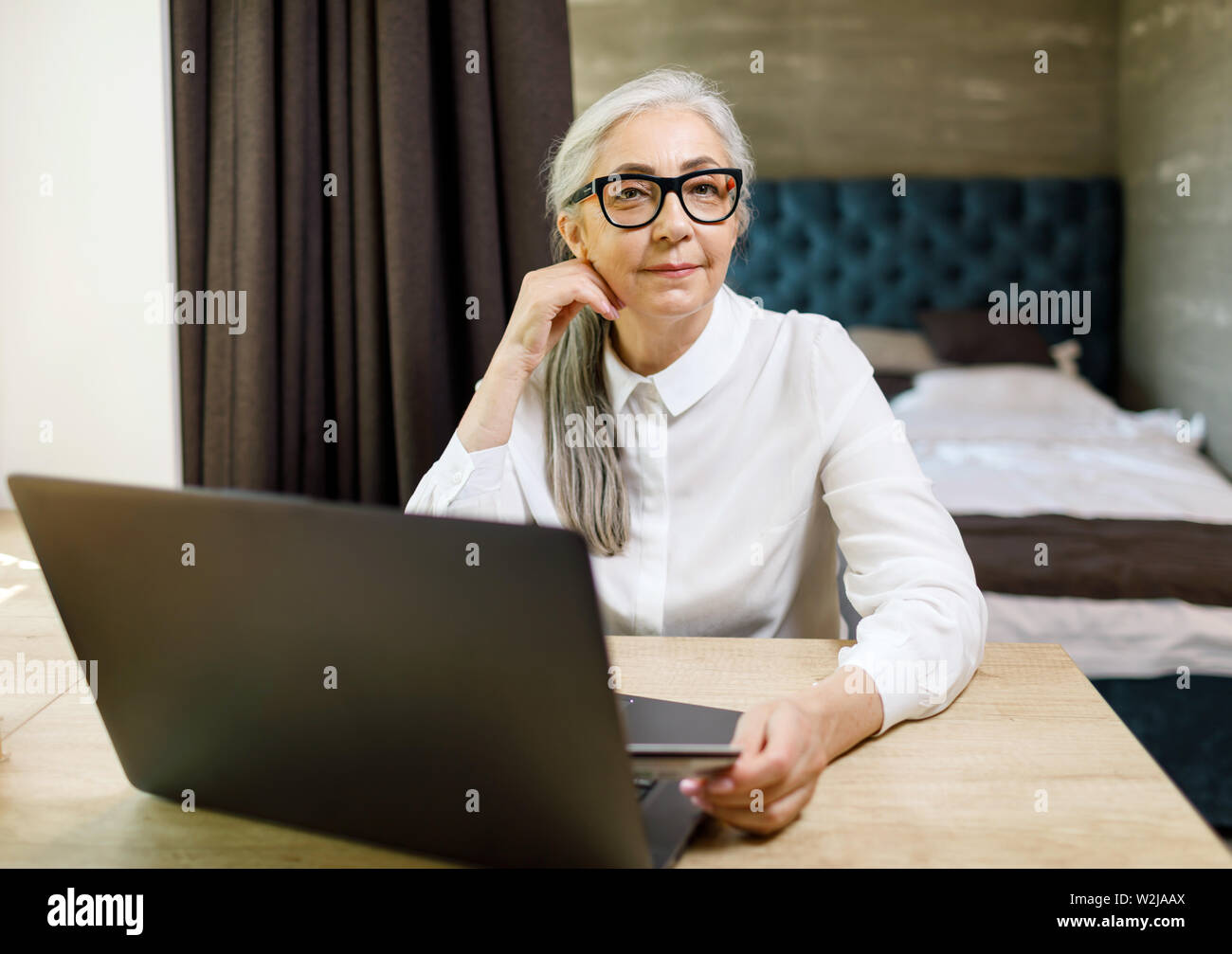 Senior langhaarige Frau Brille sitzt mit Laptop am Tisch in Ihrem komfortablen Wohnung Stockfoto