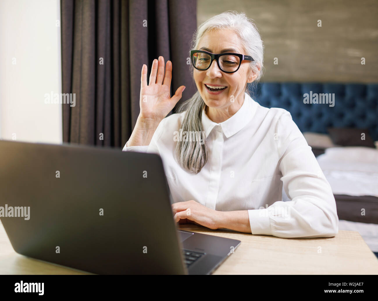Senior langhaarige Frau Brille Winken mit der Hand während sie Familie videochat Programm auf dem Laptop Stockfoto