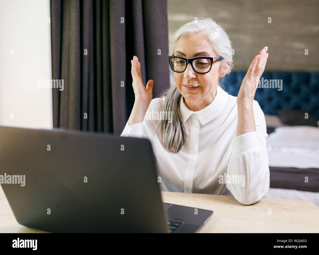 Senior langhaarige Frau Brille sitzt an ihrer Wohnung und auf dem Laptop mit Emotionen überrascht, schockiert Stockfoto