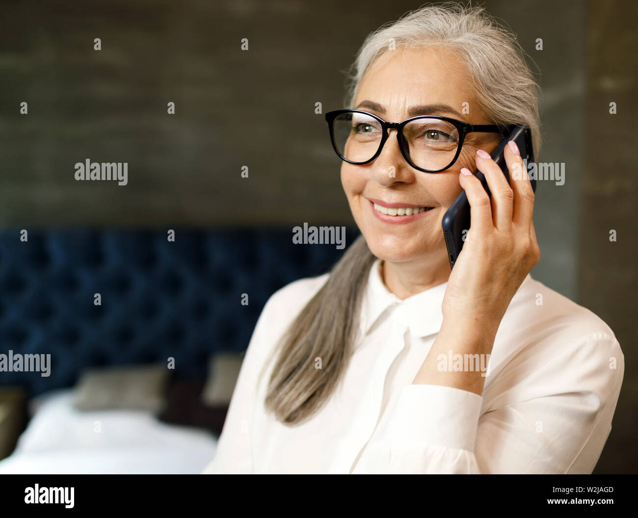 Lächelnde ältere Frau mit grauen Haaren sprechen auf dem Smartphone mit positiven Emotionen Stockfoto