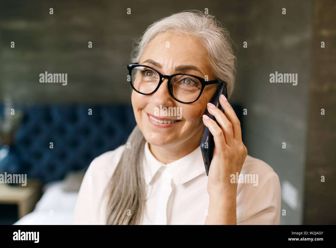 Lächelnde ältere Frau mit weißen Haaren in Brillen sprechen auf dem Smartphone Stockfoto