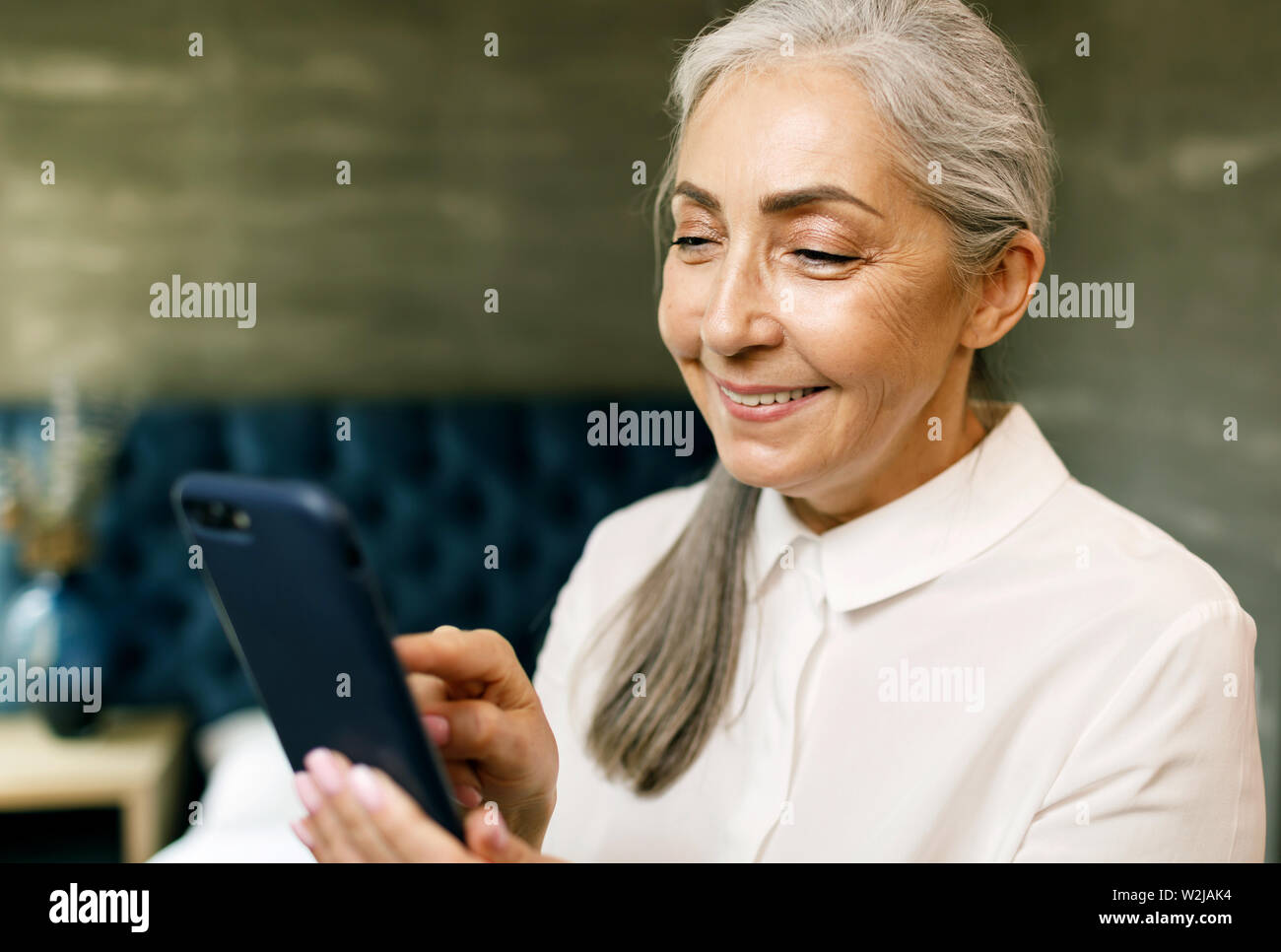 Ältere Frau mit grauen Haaren holding Smartphone und lächelnd Stockfoto