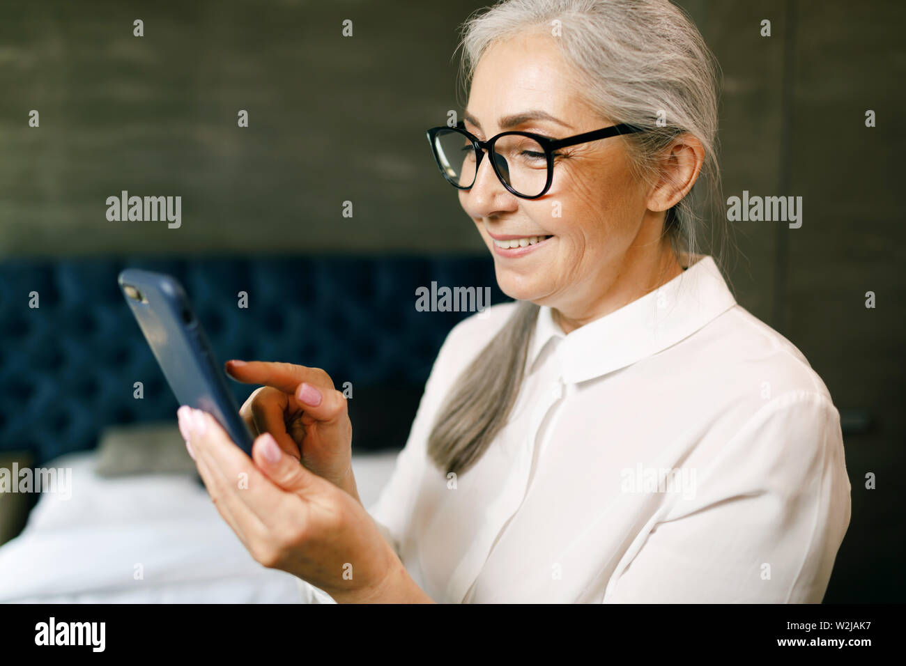 Ältere Frau mit grauen Haaren in Brillen eingeben Nachricht auf dem Smartphone Stockfoto
