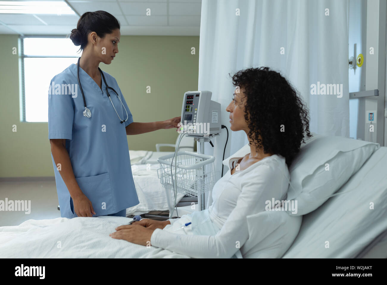 Ärztin Medical Monitor einstellen, während die weiblichen Patienten sitzen auf dem Bett in der Gemeinde Stockfoto