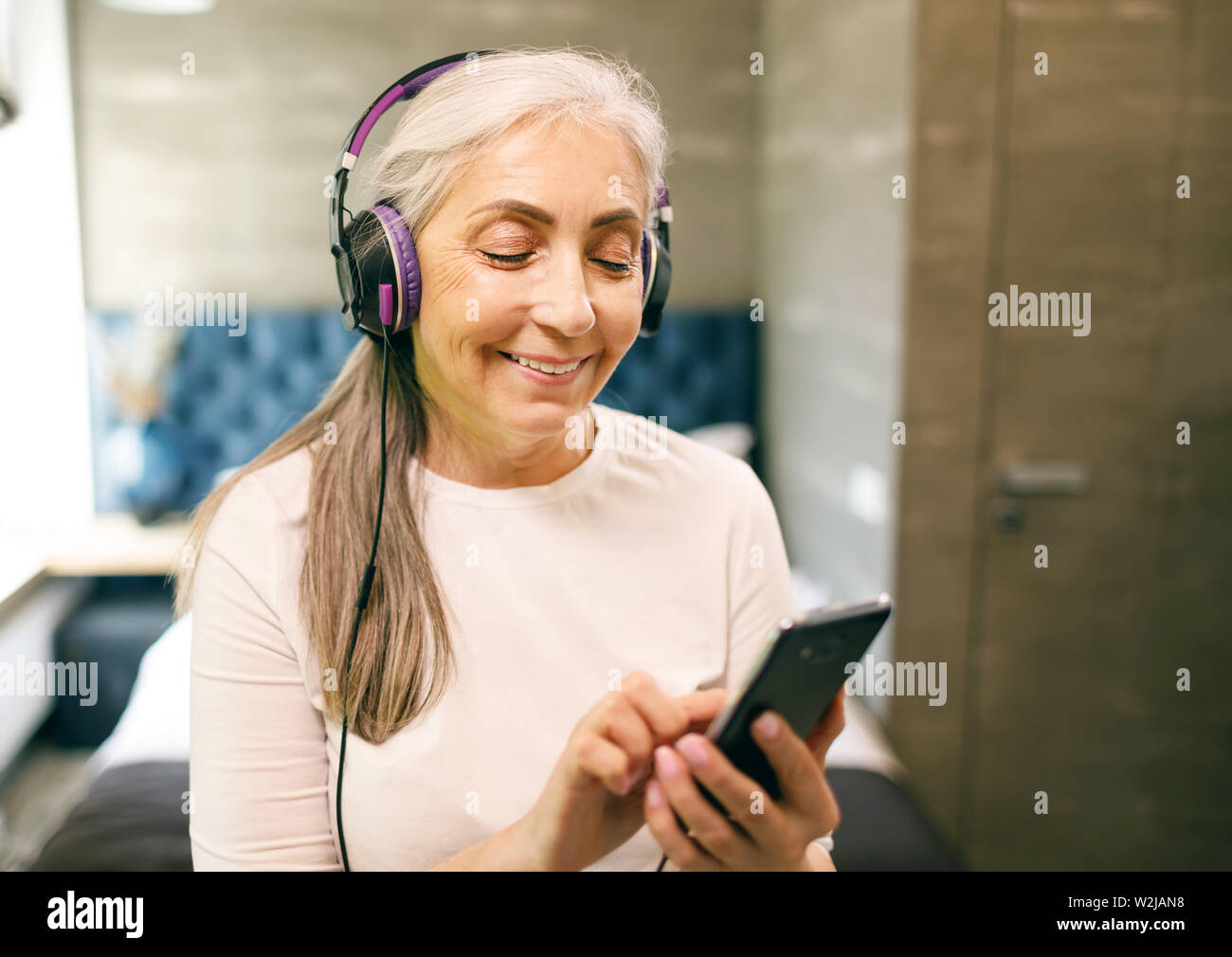 Ältere Frau mit weißen Haaren in Kopfhörer schalten Sie Musik auf dem Smartphone Stockfoto