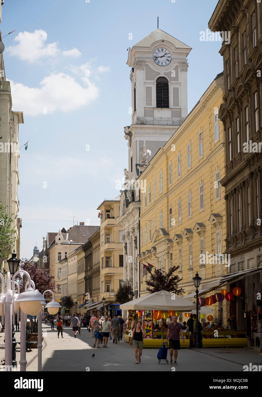 Street Scene auf Vaci Utca mit dem Turm der katholischen Kirche von Budapesti Belvárosi Szent Mihály-templom Stockfoto