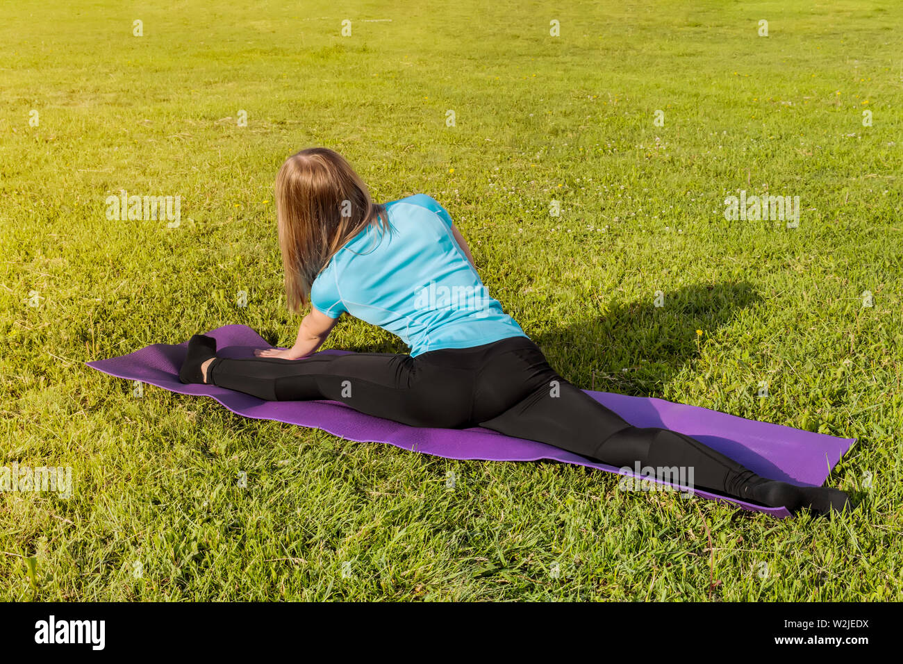 Eine Frau, die Trainer in einem sportlichen kurzen Top und Fitnessraum leggings macht eine breite Garn auf der Wolldecke für Yoga Hände werden nach oben gerichtet auf die Yogamatte angehoben, im Sommer Stockfoto