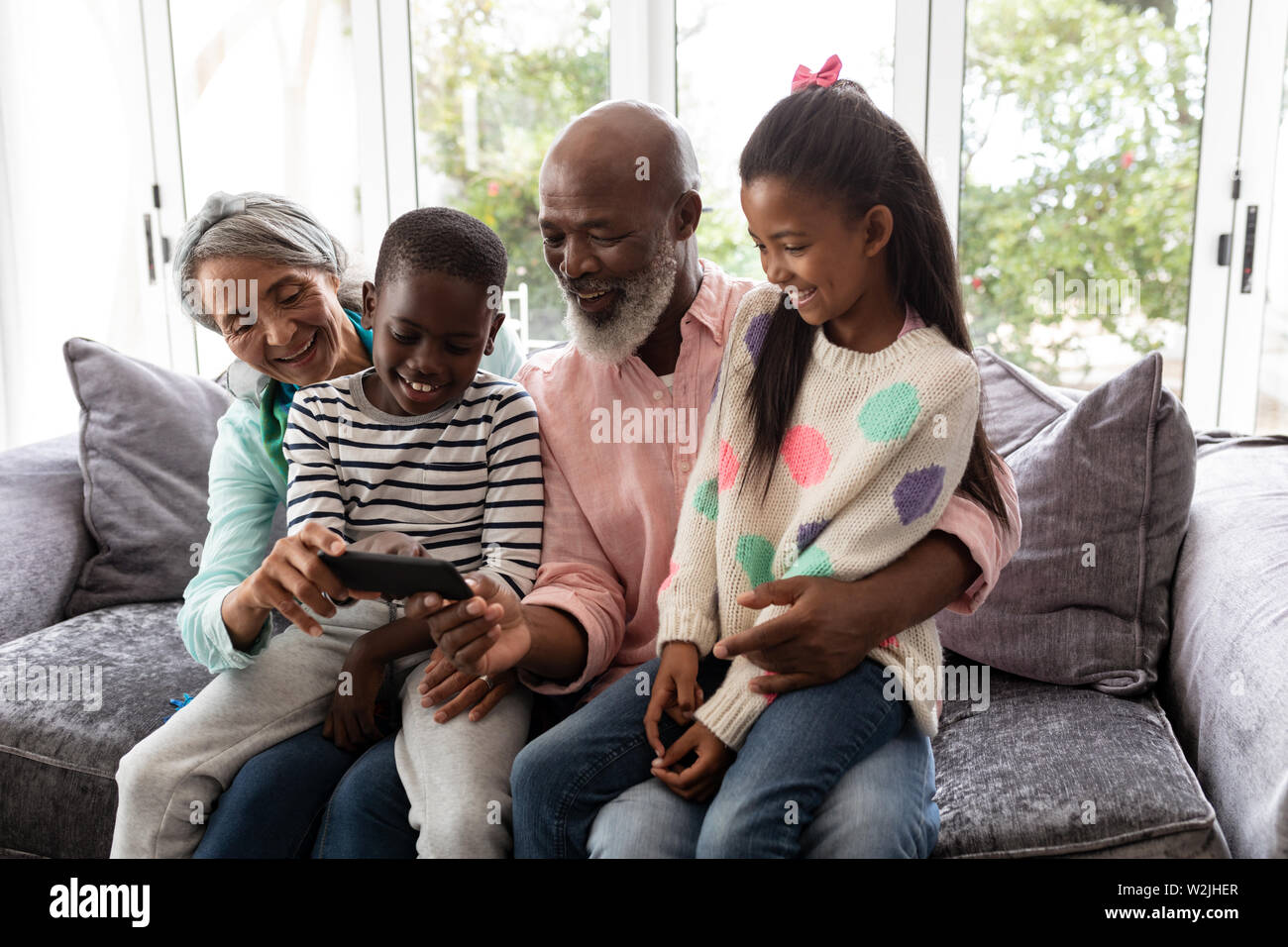 Multi-Generation, Familie das Betrachten von Fotos auf Handy im Wohnzimmer Stockfoto