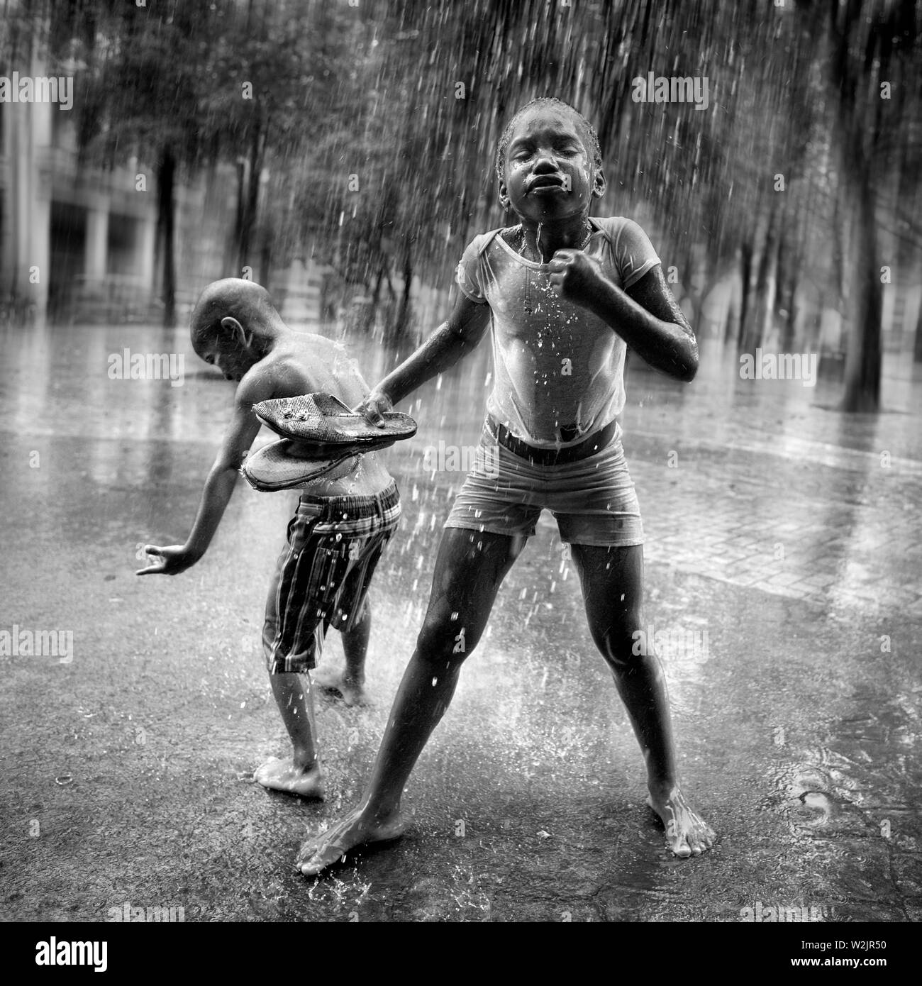 Kinder spielen unter Wasser von den Dächern in einem sintflutartigen Regen entladen. Stockfoto