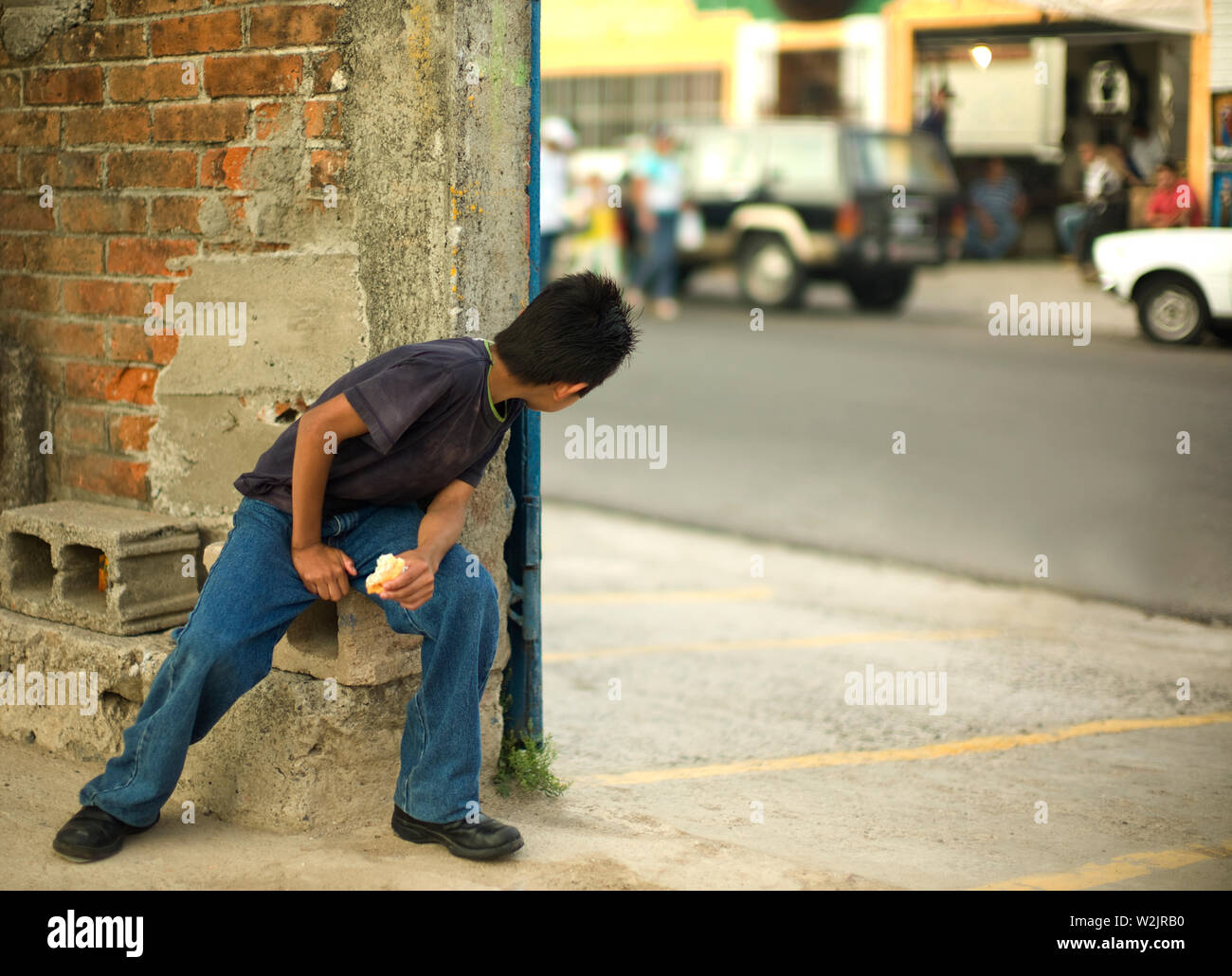 Junge sitzt auf einer konkreten Brink Kollegen um die Ecke eines Gebäudes. Stockfoto