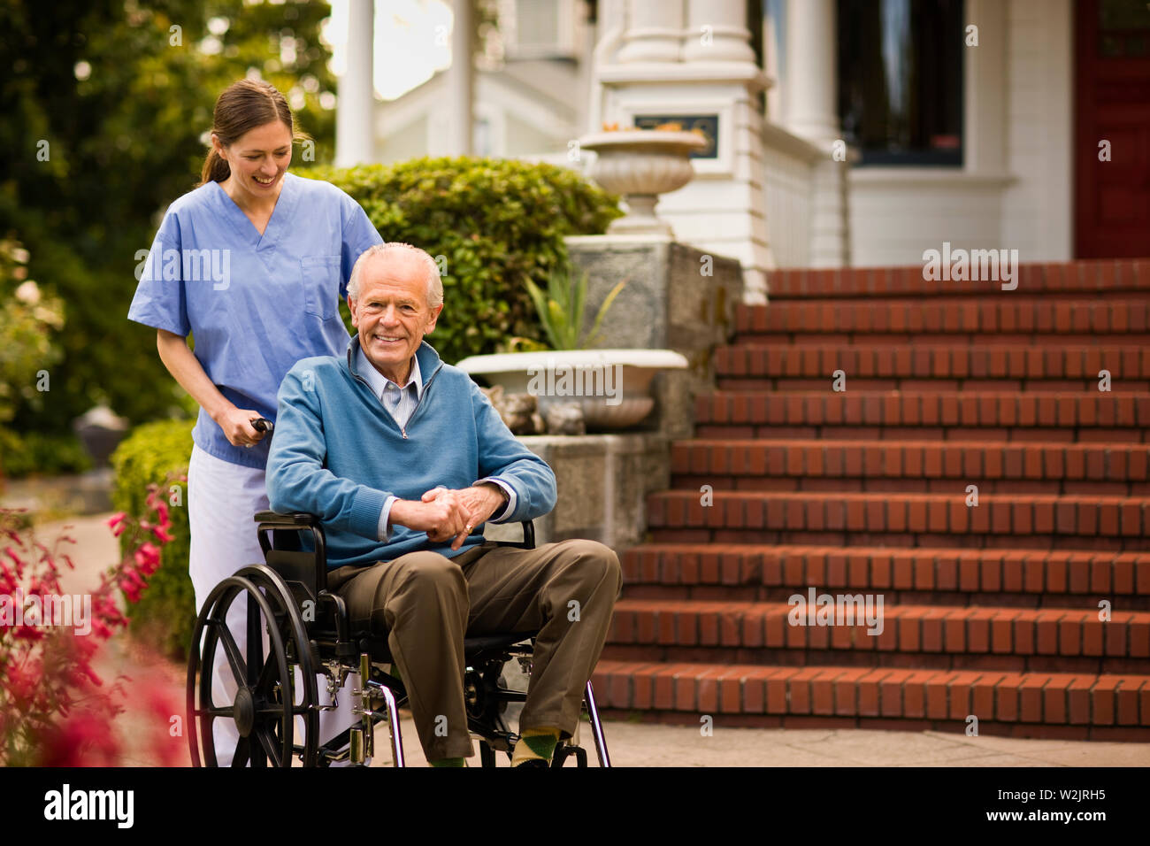 Junge Krankenschwester drückt älterer Mann im Rollstuhl. Stockfoto