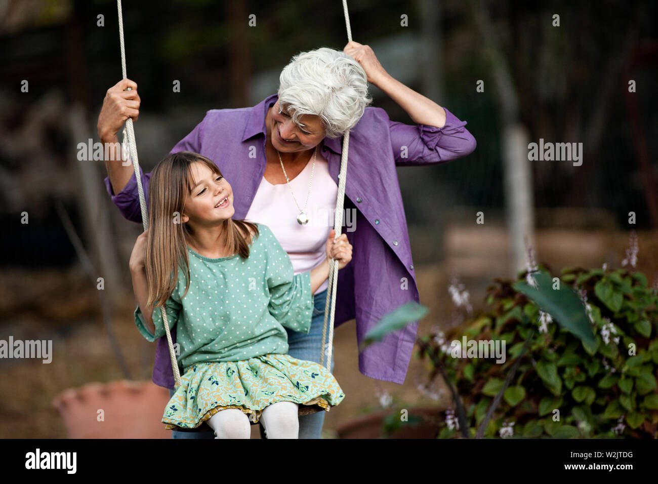 Ältere Frau schiebt ihre Enkelin auf einer Schaukel. Stockfoto