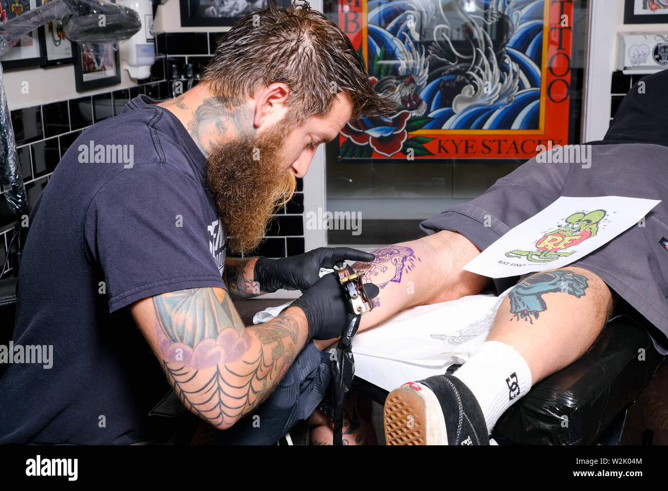 Ein tätowierer oder Tattoo Künstler arbeitet auf einem Client eine Tätowierung oder ein Stück der Body Art mit einem elektrischen Tattoo Maschine. Stockfoto