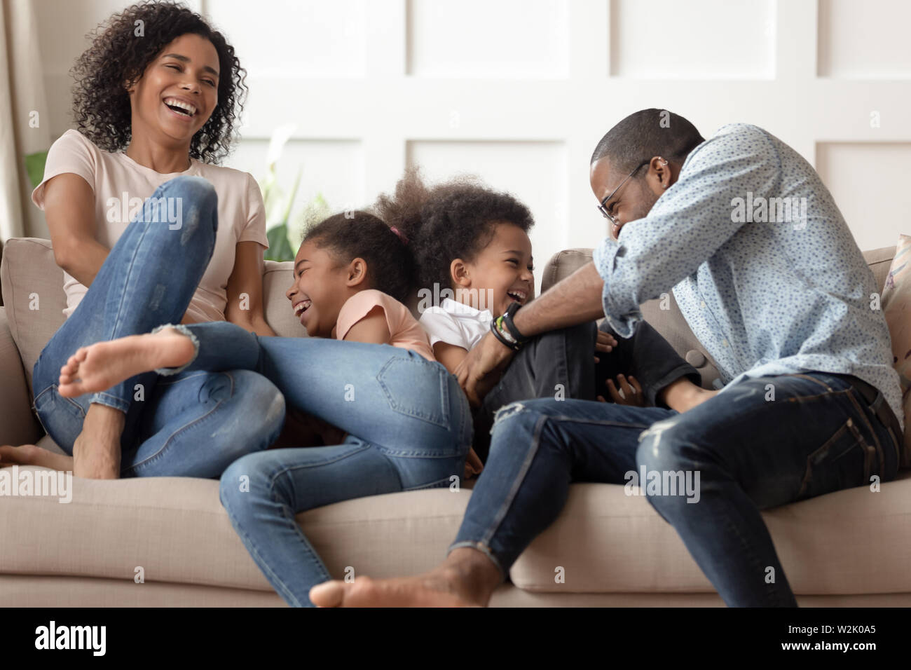 Gerne afrikanische Familie mit Kindern kitzeln zum Lachen sitzen auf dem Sofa Stockfoto