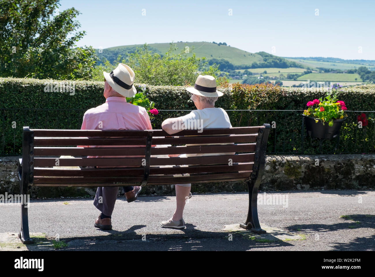 Ältere Rentnerehepaar entspannen auf einer Parkbank, die an der Ansicht von Blackmore Vale in Shaftesbury, Dorset Stockfoto