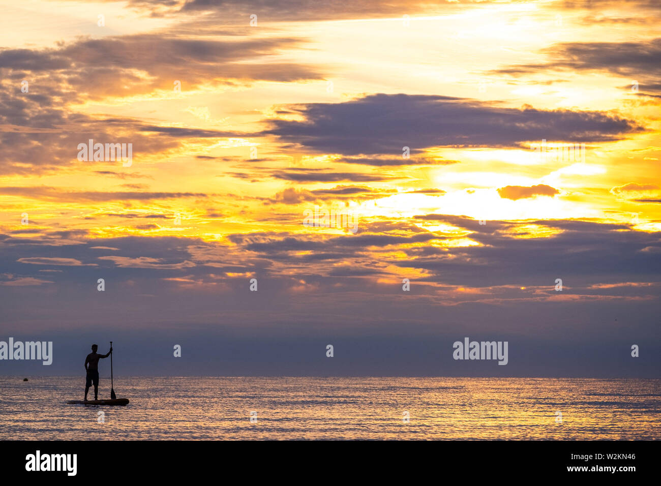 Aberystwyth Wales UK, Dienstag, 09. Juli 2019 UK Wetter: ein Mann gegen die Farben des Sonnenuntergangs paddleboard Silhouette, wie Sie auf dem ruhigen Meer vom Strand aus in Aberystwyth am Ende eines warmen Sommern Tag in West Wales. Photo Credit: Keith Morris // Alamy leben Nachrichten Stockfoto