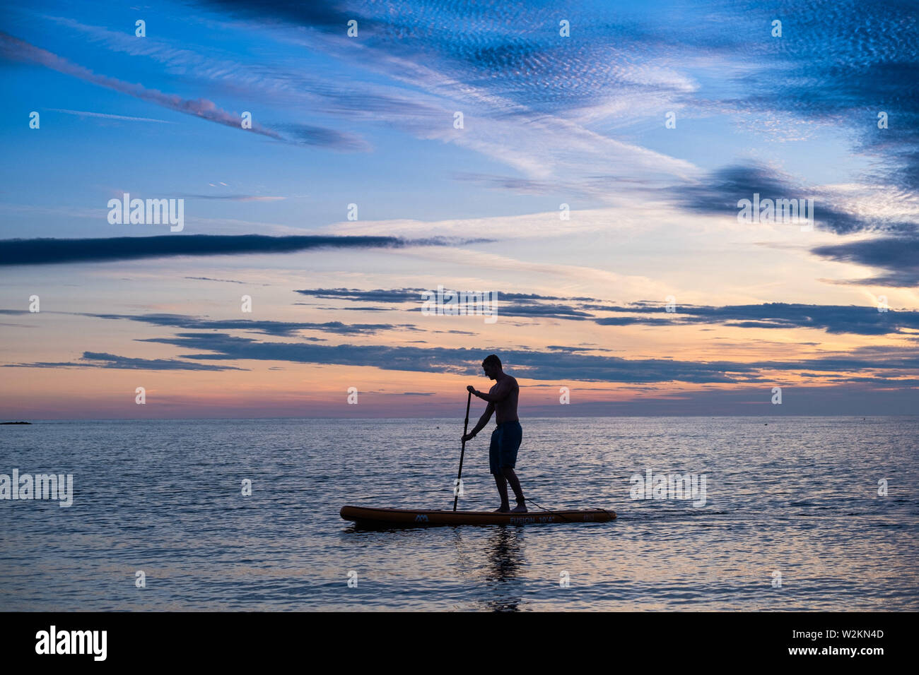 Aberystwyth Wales UK, Dienstag, 09. Juli 2019 UK Wetter: ein Mann gegen die Farben des Sonnenuntergangs paddleboard Silhouette, wie Sie auf dem ruhigen Meer vom Strand aus in Aberystwyth am Ende eines warmen Sommern Tag in West Wales. Photo Credit: Keith Morris // Alamy leben Nachrichten Stockfoto