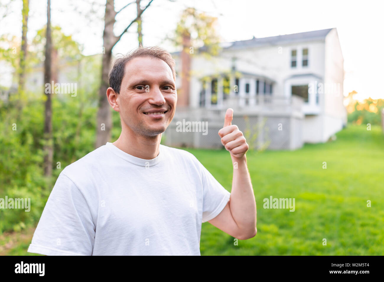 Junger Mann glückliche Eigenheimbesitzer in Herndon, Virginia, Fairfax County Wohngegend im Frühjahr oder Sommer Haus Hinterhof zeigt mit Thum Stockfoto