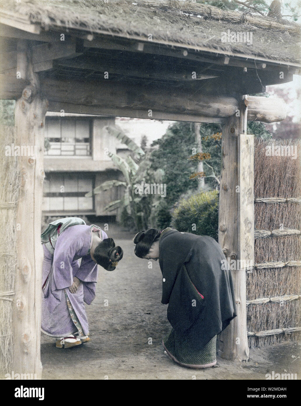 [1880s Japan - Japanische Frauen Begrüßung am Tor] - Zwei junge japanische Frauen im Kimono und traditionellen Kopfbedeckungen Bug am Gate eines privaten Hauses. 19 Vintage albumen Foto. Stockfoto
