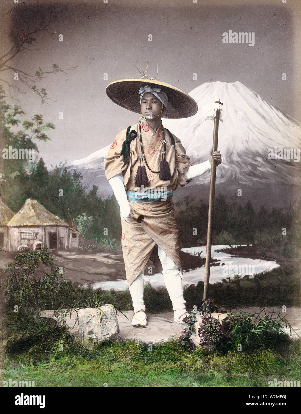 [ 1880er Japan - Japanese Pilgrim ] - EIN Studiofoto eines Pilgers, der für die Pilgerfahrt zum Mt. Fuji. Er trägt einen langen, hölzernen Staf und eine Glocke und trägt einen konischen Hut. Die Glocke wurde benutzt, um den Pilger daran zu erinnern, dass das Leben kurz und vergänglich war. Es half auch, wilde Tiere wie Bären zu erschrecken. Vintage Albumin Foto des 19. Jahrhunderts. Stockfoto