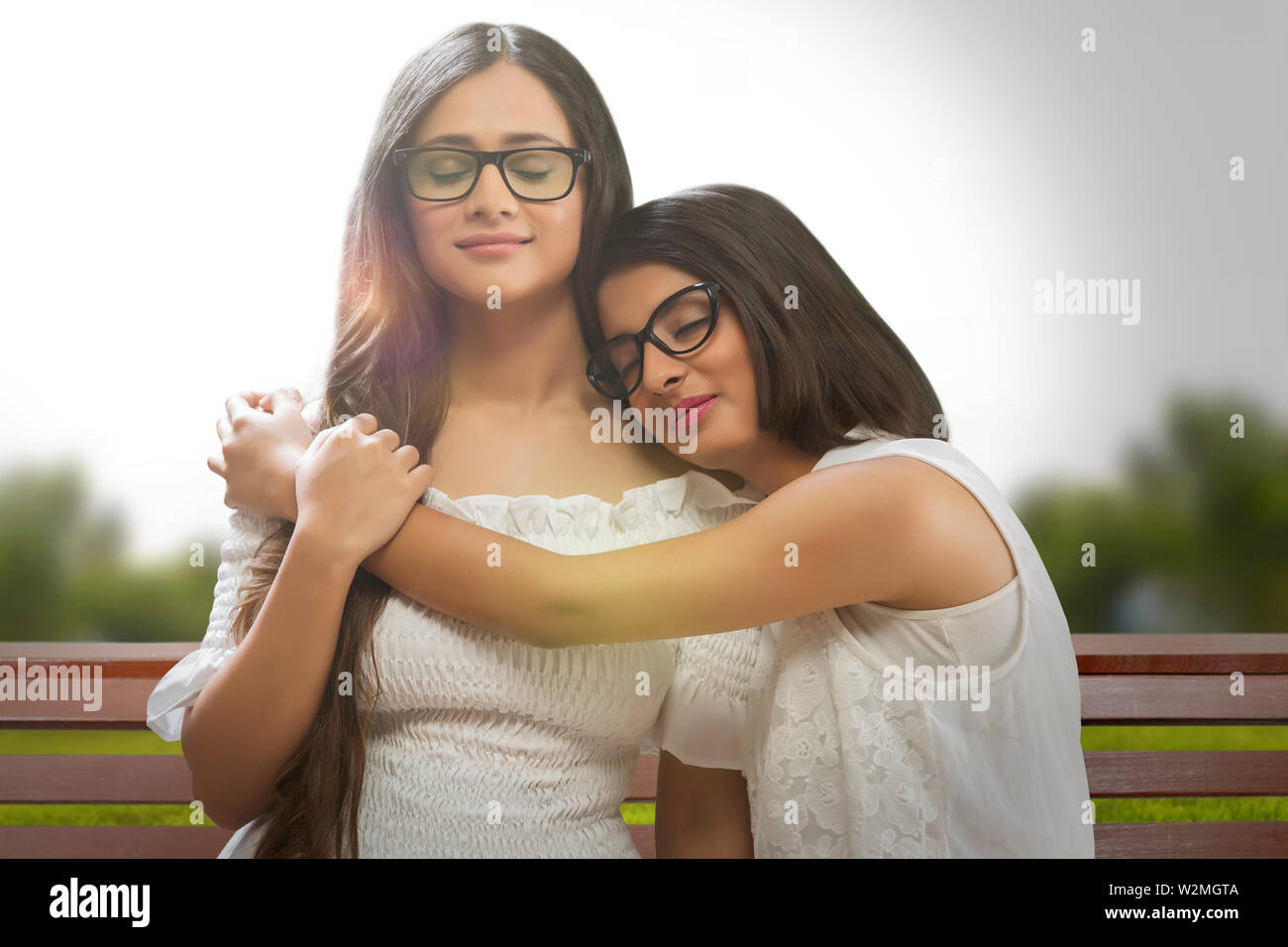 Junge Mädchen in Brillen stehen mit ihrer Freundin, die Arme um sie und Kopf auf die Schulter und die Augen geschlossen. Stockfoto