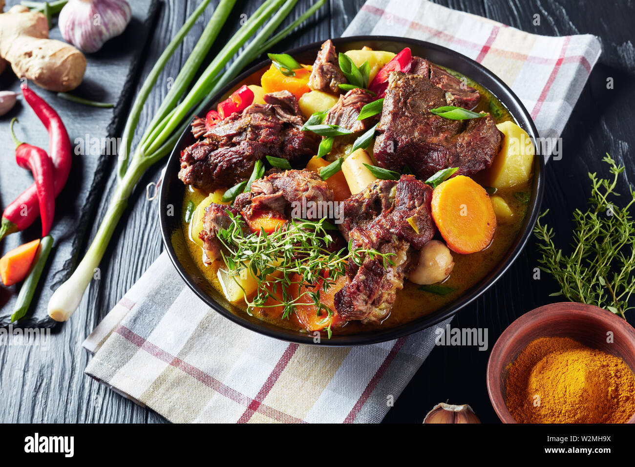 Traditionellen jamaikanischen Curry Goat - langsam gekocht Jamaikanischen gewürztem Fleisch und Gemüse würzige Curry in einem schwarzen Schüssel auf einem rustikalen Holztisch, close-up Stockfoto