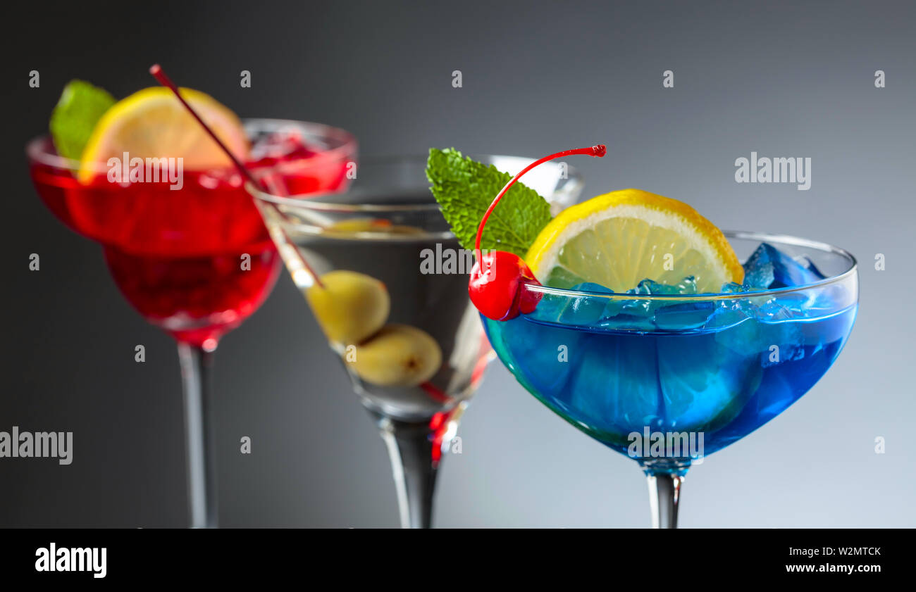 Zwei bunte Cocktails und Dry Martini mit grünen Oliven. Rote und blaue Cocktails mit Eis, Zitrone, Minze und Kirsche. Stockfoto