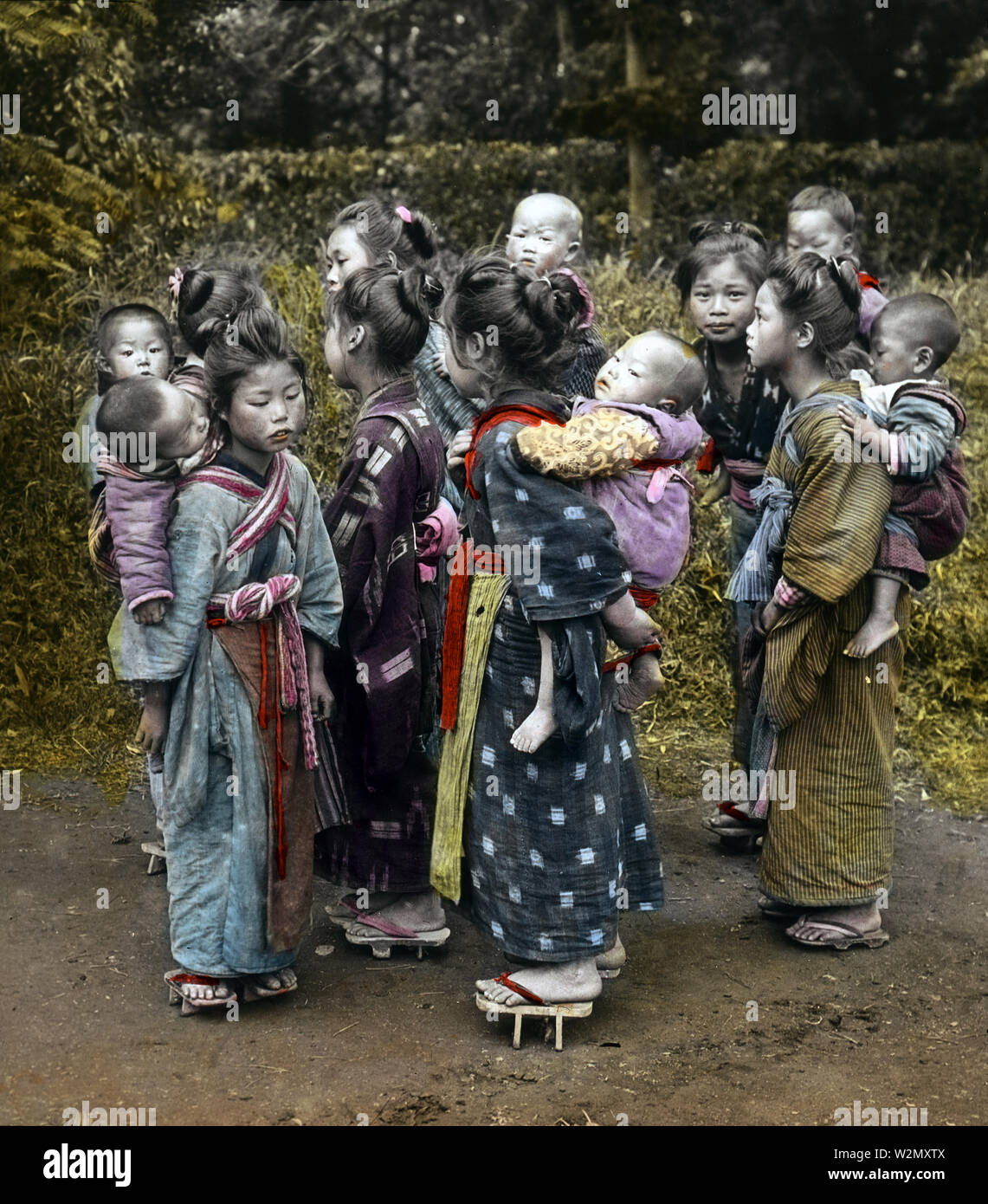 [1900s Japan - Junge japanische Mädchen tragen Babys] - Eine Gruppe von komori auf der Landstraße in den frühen 1900er Jahren. Komori waren junge Mädchen aus armen Familien, die durch das Jahr angestellt wurden Mittel- und Oberschicht die Mütter in der Pflege ihrer Kinder zu unterstützen. Zusätzlich zum Tragen das Baby herum, die komori würde auch ein wenig mit der Hausarbeit unterstützen. Komori erhielt Nahrung, Unterkunft, Kleidung, und gelegentlich etwas Geld. 1900-1903 datiert von Enami Spezialist Rob Oechsle. 20. Jahrhundert vintage Glas schieben. Stockfoto