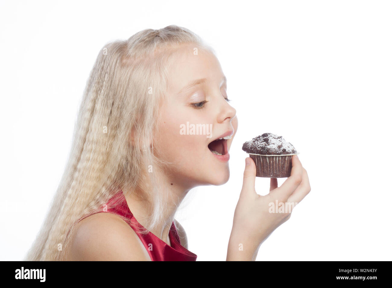Mädchen beißen einen Schokoladenkuchen auf weißem Hintergrund. Stockfoto