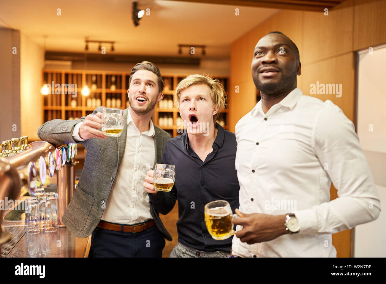 Drei Männer, die als Fans in einem Pub oder Kneipe spannendes Fußballspiel schauen Stockfoto