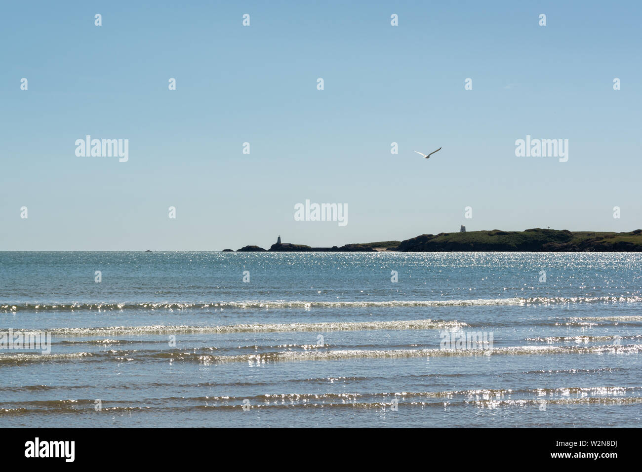 Hartes Sonnenlicht Reflexion über die Wellen im Meer und Llanddwyn Island im Hintergrund Stockfoto